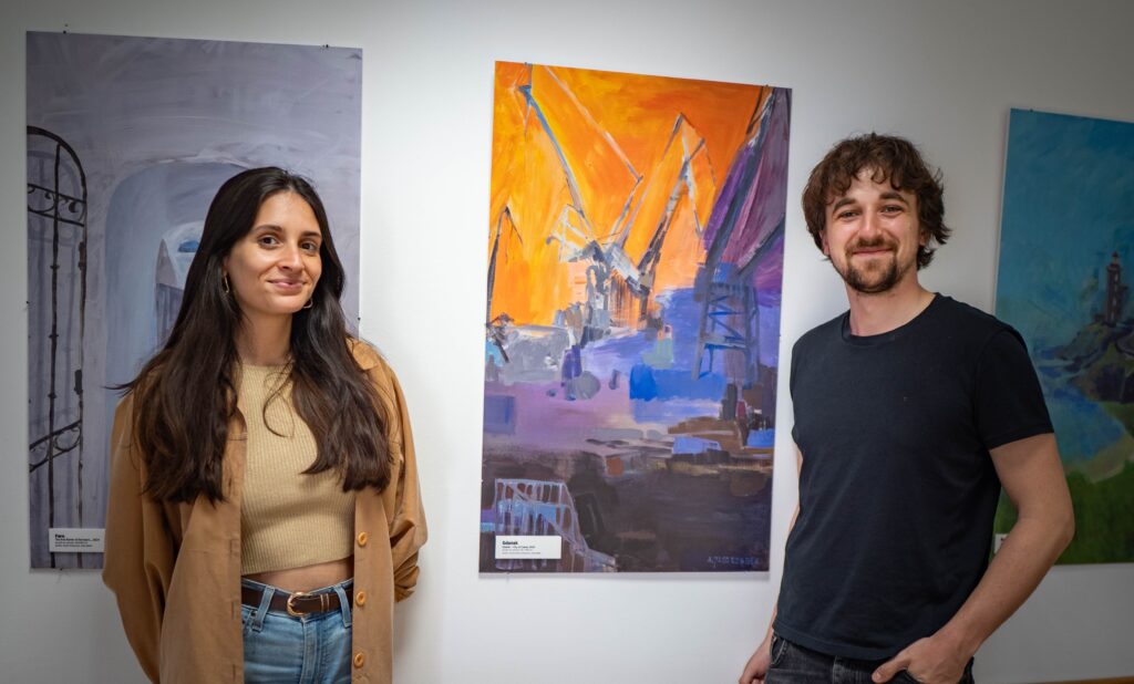 Joana and Marcel during the job shadowing, with artworks representing their respective cities in the background.