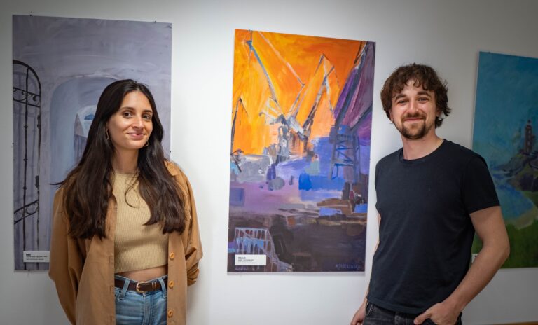 Joana and Marcel during the job shadowing, with artworks representing their respective cities in the background.