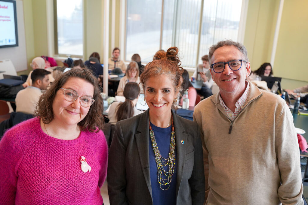 Two women and a man in front of people in a meeting room