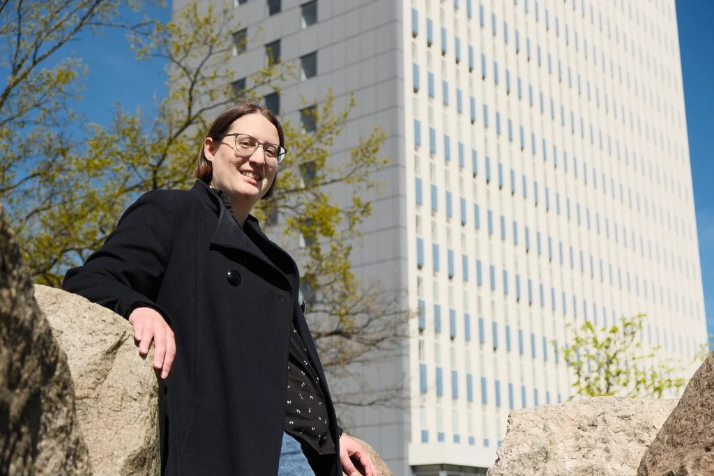 A person looks into the camera standing in front of a tall building